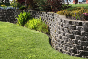 Well landscaped wall of cement cobblestone bricks with grass and ornamental plants