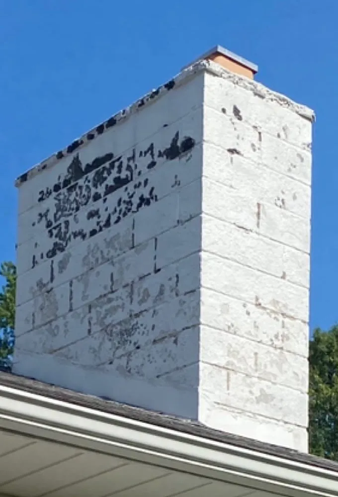 Painted concrete block chimney with peeling paint and crumbling faces before rebuild