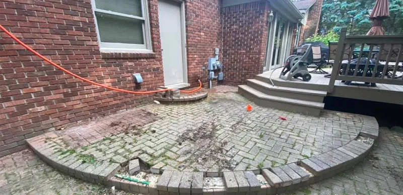 Crumbling herringbone paver patio with a broken curved border before repair