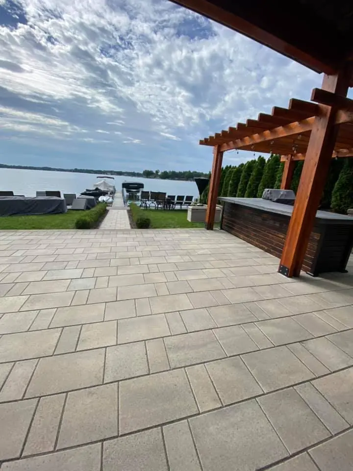 Large-format paver patio under a cedar pergola with an outdoor kitchen and lake view